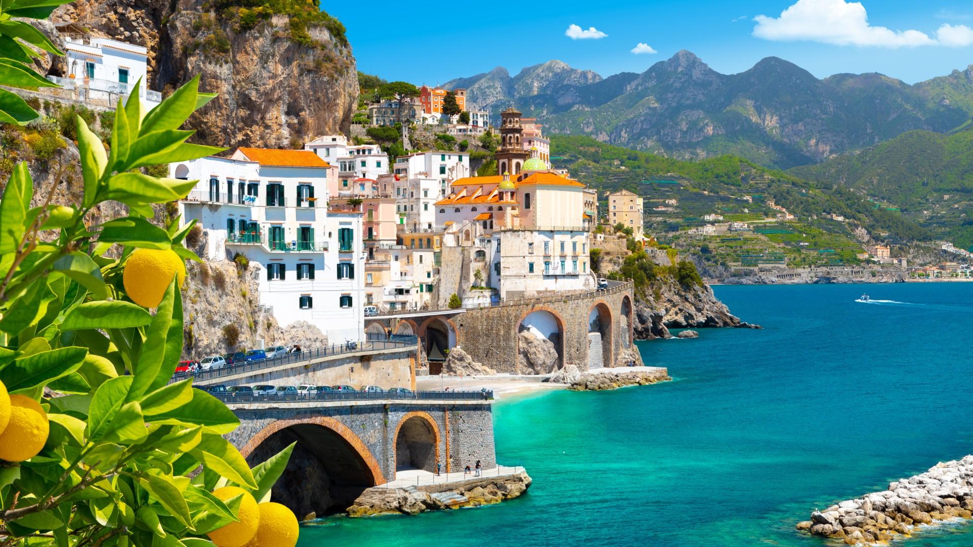 Coastal view with colorful houses and lemons, turquoise sea and mountains in the background.