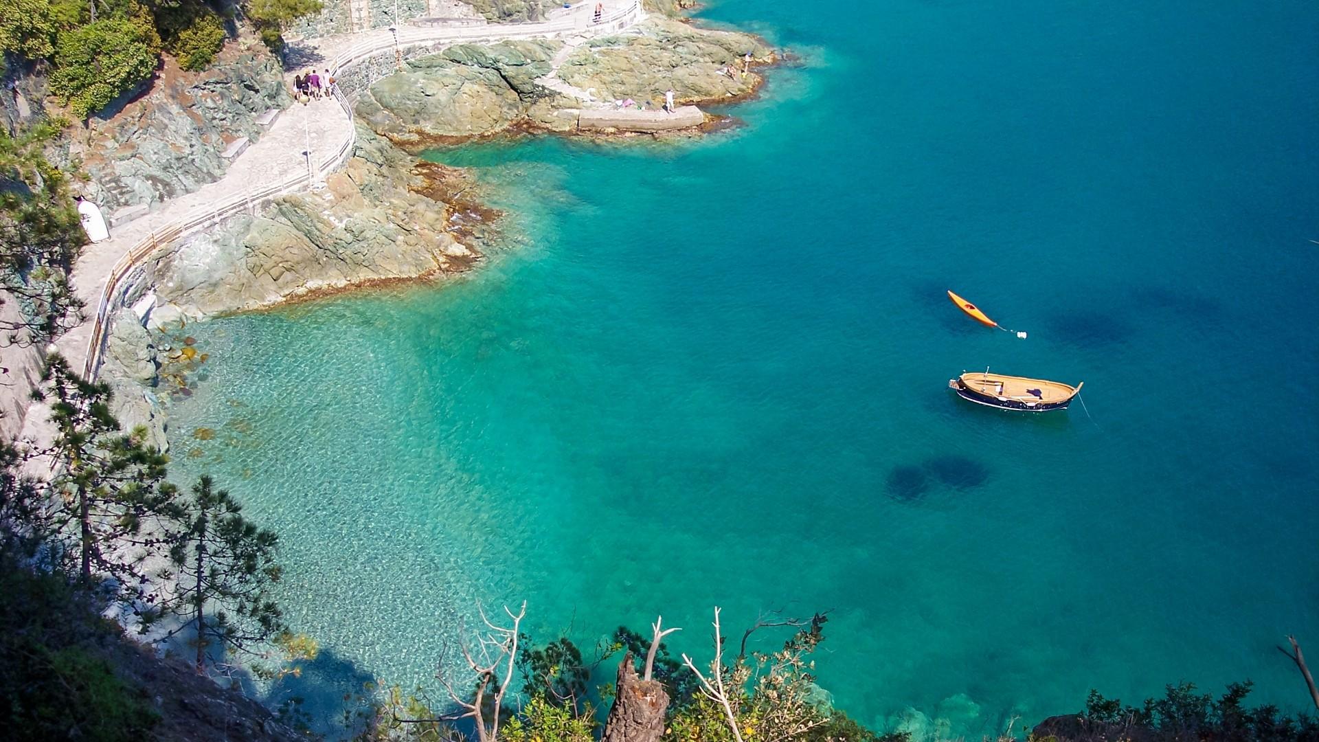 Coastal path with boats on crystal clear waters.