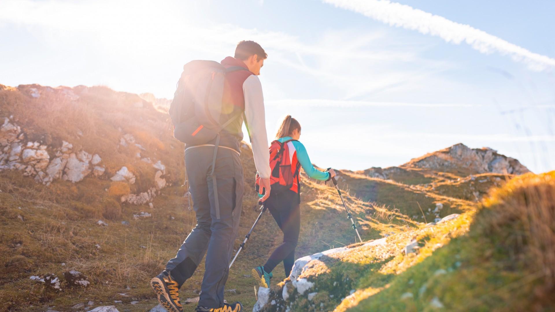 Deux personnes randonnent sur un sentier de montagne au coucher du soleil.