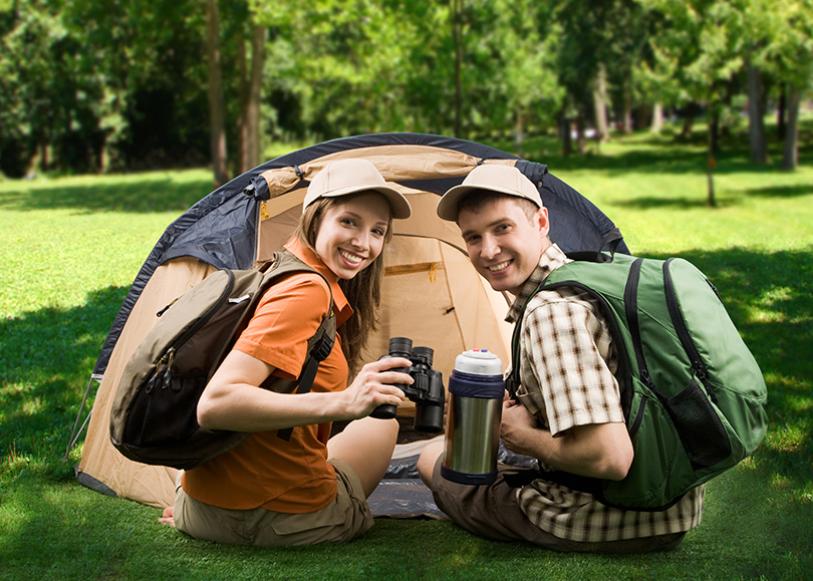 Zwei Personen campen mit Rucksäcken und Ferngläsern vor einem Zelt.