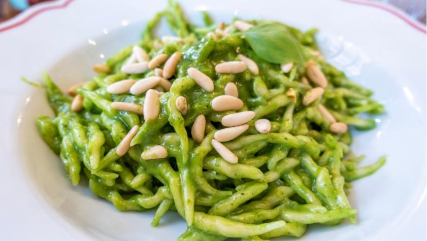 Trofie with pesto and pine nuts on white plate.