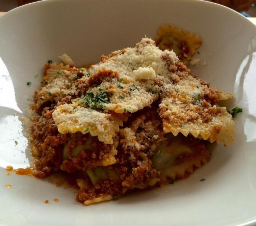 Ravioli with meat sauce and grated parmesan in a white bowl.