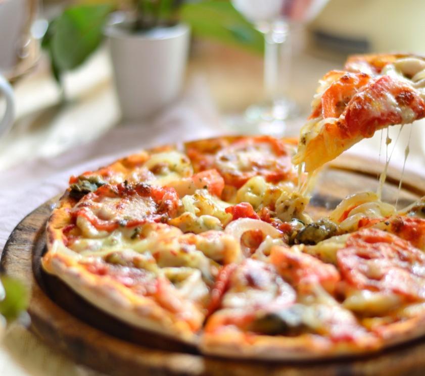 Pizza with cheese, tomato, and vegetables on a wooden board.