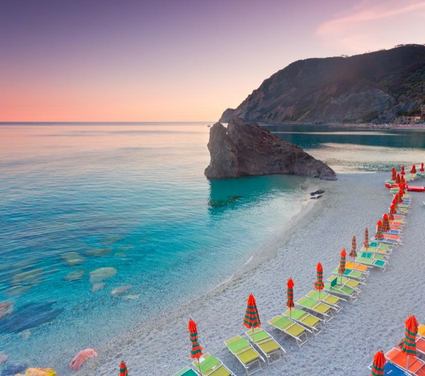 Ruhiger Strand mit bunten Liegen und Sonnenschirmen, kristallklarem Meer und Klippen.