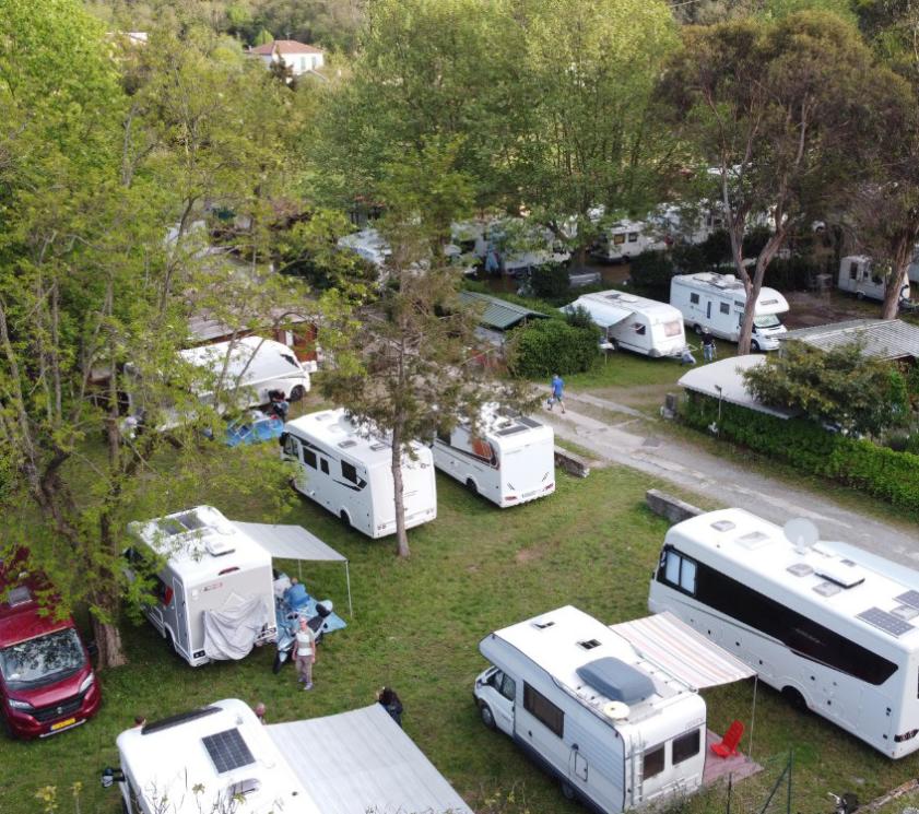 Campsite with motorhomes and caravans, surrounded by nature.