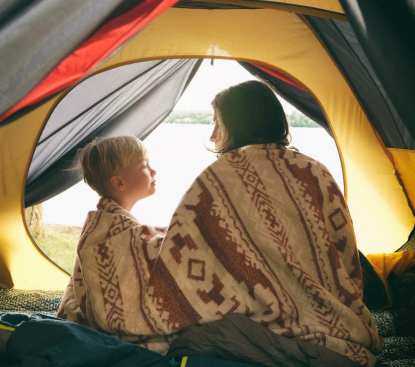Two people in a tent, wrapped in a blanket, looking outside.