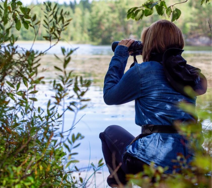 Person observing nature with binoculars near a lake.
