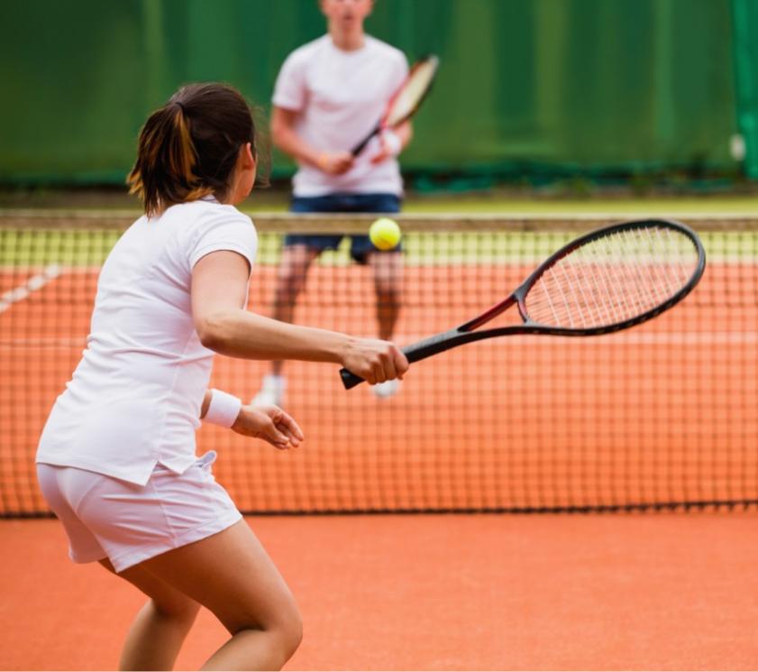 Two people playing tennis on a clay court.